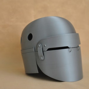 Könnte beinhalten: Ein grauer Helm mit Visier und einem kleinen Loch oben. Der Helm ist aus glattem, hartem Material.