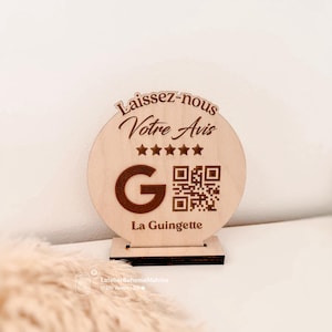 Puede incluir: Una taza de cerámica blanca con asa negra y el texto "But First, Coffee" en negrita negra. La taza se encuentra sobre un fondo borroso, sugiriendo un ambiente acogedor.