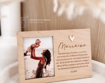 May include: A rectangular light wood photo frame featuring a photograph of a person lifting a baby on a beach. The frame includes a small pink heart icon and French text that reads: Marraine, Ma marraine d'amour, tu es une personne de confiance choisie par mes parents pour ton grand coeur et sur qui je pourrais toujours compter. Merci d'être toujours présente dans les moments importants de ma vie, ALINE.