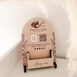 Könnte beinhalten: Hölzerner Salon-Display-Ständer mit dem Text "Urban Chic Salon" und einem Logo einer Frauensilhouette mit Schere. Der Ständer hat einen Schlitz für Karten und ist mit floralen Designs und dem Text "Servez-vous" verziert.