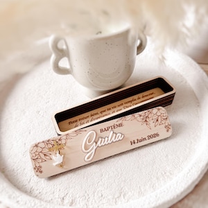 Peut inclure: Une boîte rectangulaire en bois avec un couvercle amovible gravé de motifs floraux, une croix dorée, une colombe blanche et le texte "BAPTÊME Giulia 14 Juin 2026". L'intérieur est gravé du texte "Petit trésor béni, que ta vie soit remplie de douceur, de foi et d'espérance, et que Dieu t'accompagne."