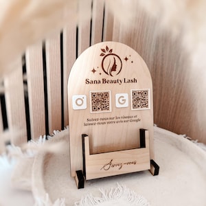 Peut inclure: Un panneau en bois clair en forme d'arche avec le logo Sana Beauty Lash, deux codes QR et des icônes de réseaux sociaux. Le texte indique : Sana Beauty Lash, Suivez-nous sur les réseaux et laissez-nous votre avis sur Google, et Servez-vous.