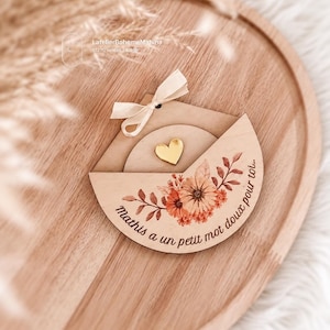 Peut inclure: Un ornement en bois en forme d'enveloppe semi-circulaire avec une illustration florale dans des tons orange et marron, le texte "Mathis a un petit mot doux pour toi...", un petit cœur doré et un nœud en ruban de couleur crème.