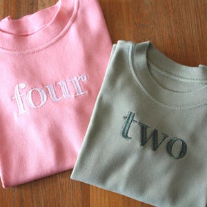 May include: Two pink and green t-shirts with the numbers "four" and "two" embroidered on them.