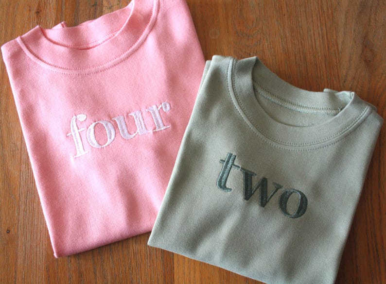 May include: Two pink and green t-shirts with the numbers "four" and "two" embroidered on them.