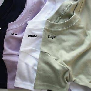 May include: Four t-shirts in different colours: navy, lilac, white, and sage. The shirts are folded and laid out side-by-side. The colours are labelled below each shirt.