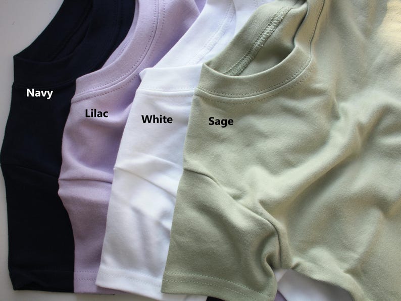May include: Four t-shirts in different colours: navy, lilac, white, and sage. The shirts are folded and laid out side-by-side. The colours are labelled below each shirt.