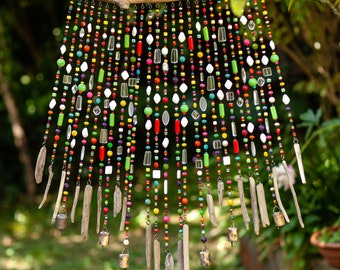 May include: A colorful beaded wind chime with driftwood accents and small bells. The beads are in various colors, including red, green, blue, and yellow. The driftwood is natural and has a rustic look. The bells are silver and add a gentle sound to the wind chime.