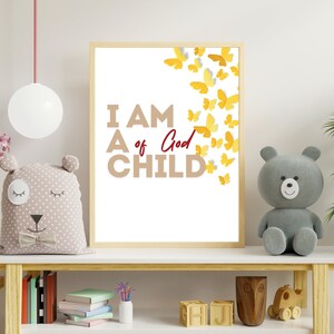 May include: A framed print with the text "I AM A CHILD of God" in brown letters with a red "God". Yellow paper butterflies are scattered around the text. The print is hanging on a white wall above a wooden shelf.