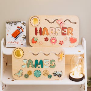 May include: Two wooden name puzzles, one with the name "HARPER" in colorful letters and decorative shapes, and the other with "JAMES". A children's book titled "Little Red Sleigh" is also visible.