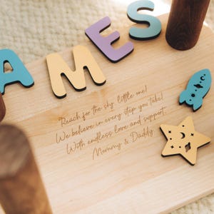 Puede incluir: Un taburete de madera clara con el nombre JAMES en letras recortadas de colores. La superficie est&aacute; grabada con el texto: Reach for the sky, little one! We believe in every step you take! With endless love and support. Mommy & Daddy. Incluye un cohete azul y una estrella amarilla recortados.