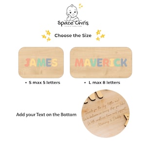 Puede incluir: Un letrero de madera con el logotipo de Space Chris, dos tablas rectangulares con los nombres JAMES y MAVERICK en letras pastel, y un recuadro circular que muestra texto grabado personalizado Reach for the sky, little one!