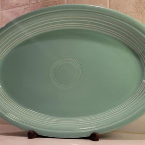 May include: An oval-shaped serving platter in a light seafoam green color. The platter features a smooth, glossy finish with a series of concentric circular ridges embossed along the wide rim and a single circular ring centered in the middle.