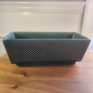 May include: A rectangular ceramic planter with a dark green exterior featuring a raised diamond grid pattern. The interior of the vessel is a smooth, solid dark green finish, and the base is slightly recessed with a flat bottom edge.