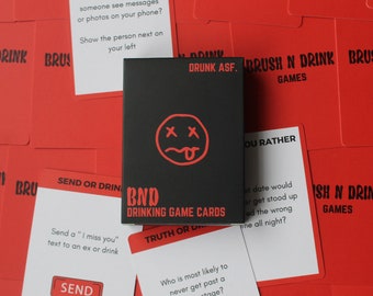 May include: A black card with a white smiley face with red eyes and tongue sticking out. The card says "BND Drinking Game Cards" in white text. The card is surrounded by red cards with white text. Some of the text on the red cards includes "Would You Rather", "Send or Drink", "Truth or Dare", and "Brush N Drink Games".