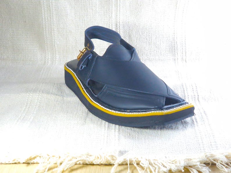 May include: A navy blue sandal with a strap and buckle closure. The sandal has a black sole with a yellow and white trim. The shoe is made of leather-like material and is designed for comfort and style.