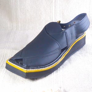 May include: A navy blue sandal with a square toe and a strap around the ankle. The sole is black with a yellow and white trim. The sandal has a leather upper and a small heel.