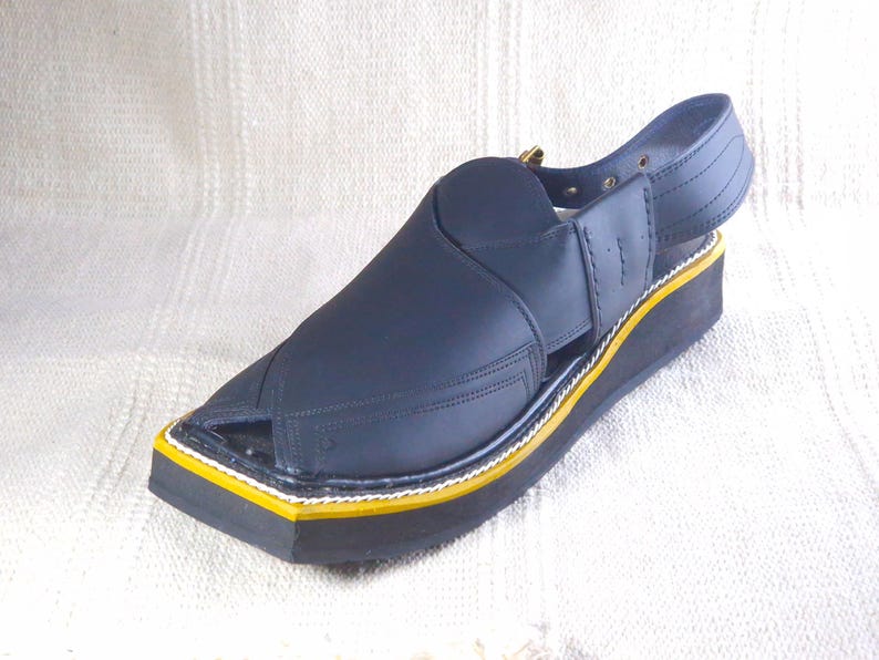 May include: A navy blue sandal with a square toe and a strap around the ankle. The sole is black with a yellow and white trim. The sandal has a leather upper and a small heel.