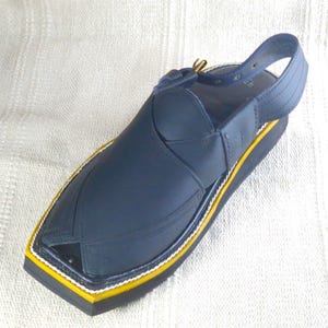 May include: A navy blue leather sandal with a strap. The sandal features a black sole with yellow and white trim. The upper part of the sandal is a solid navy blue color. The sandal is designed with a closed toe.