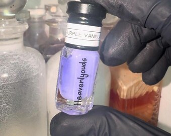 Può includere: Un piccolo flacone di vetro con un liquido viola al suo interno. Il flacone ha un tappo nero e un'etichetta bianca che dice "Purple Vanilla Heavenlyouds".