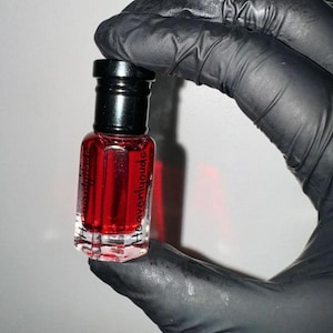 May include: A small, clear glass bottle with a black cap filled with a red liquid. The bottle is labelled "Heavenlyloude".