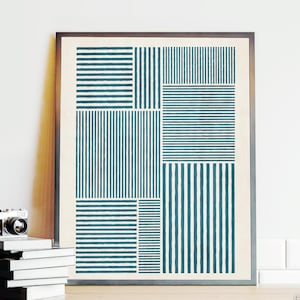 Könnte beinhalten: Gerahmter abstrakter Kunstdruck mit geometrischem Design. Das Kunstwerk zeigt türkisfarbene und weiße vertikale und horizontale Linien, die in einem Raster angeordnet sind. Eine Vintage-Kamera und ein Stapel Bücher befinden sich vor der Kunst.