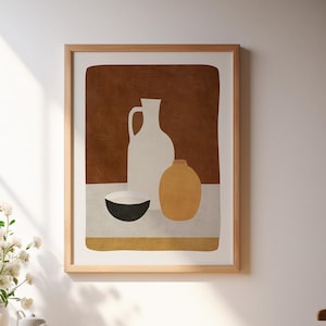 May include: A framed wall art print featuring a still life illustration of a white pitcher, a yellow vase, and a black bowl set against a deep brown background. The artwork is displayed in a light wood frame on a white wall above a wooden table.