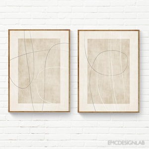May include: Two framed wall art prints featuring a beige rectangular background with thin, intersecting black and white line drawings. Each print is enclosed in a light brown wooden frame, displaying abstract, fluid, and continuous line art.