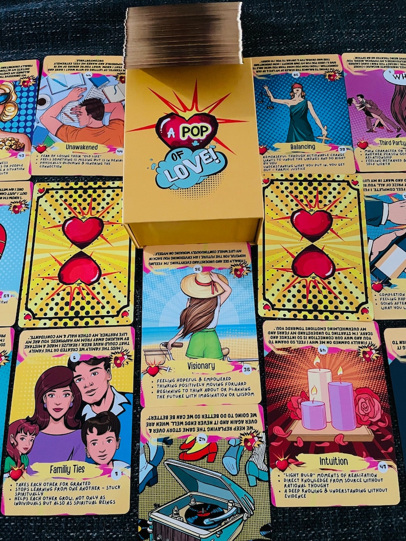 Peut inclure: Une bo&icirc;te jaune &eacute;tiquet&eacute;e A POP OF LOVE est pos&eacute;e sur un jeu de cartes pr&eacute;sentant des illustrations pop art color&eacute;es. Chaque carte affiche un titre unique, comme Visionary, Intuition ou Family Ties, accompagn&eacute; de texte et de graphismes.