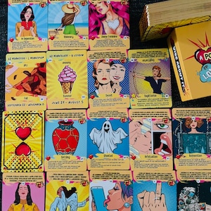 Peut inclure: Une collection de cartes oracle de style pop art pr&eacute;sentant diverses illustrations dont un c&oelig;ur bris&eacute;, un fant&ocirc;me, un cornet de glace et une personne avec une aile d'ange, avec une bo&icirc;te jaune &eacute;tiquet&eacute;e A POKE OF LOVE.