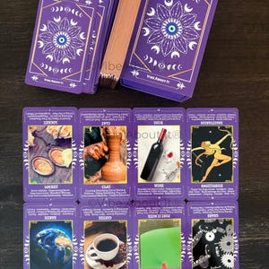 May include: A deck of purple tarot cards with a white mandala and eye design on the back. The cards feature various illustrations including a locket, a clay pot, a wine bottle, a Sagittarius figure, the Earth, a coffee cup, and mechanical gears.