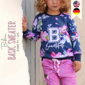Könnte beinhalten: Ein blauer, langärmliger Pullover mit Blumenmuster und einem weißen Buchstaben "B" auf der Vorderseite. Der Text "Beautiful" steht unter dem Buchstaben. Der Pullover wird von einem Kind getragen.