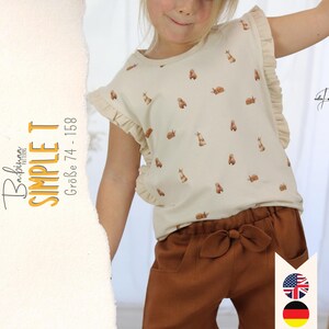 Könnte beinhalten: Ein weißes T-Shirt mit braunem Hasenprint und Rüschenärmeln. Das Shirt wird von einem Kind getragen und zu einer braunen Hose kombiniert. Der Text "Babipina Patterns SIMPLE T Größe 74 - 158" ist auf der linken Seite des Bildes sichtbar.