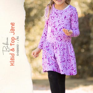 May include: A long-sleeved dress in light purple with a dark purple paint splatter pattern, featuring a drop-waist skirt and a round neckline. The text on the left reads Babinaa kleid & top jane GRÖBE80 - 146.