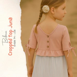 May include: A dusty pink cropped top with a V-neckline, three brown buttons down the back, and short sleeves featuring side cutouts with tied bows. The text Babinaa Cropped top Juna Größe 74 - 158 is visible on the left side of the image.