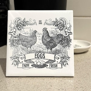 May include: White ceramic tile with a black and white illustration of two chickens and a banner that reads "EGGS FARM FRESH" with the text "EST. 1886" above the chickens.