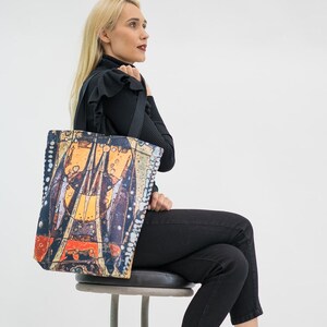 Puede incluir: Una mujer con pantalones negros y botas negras se sienta en un taburete sosteniendo una bolsa de mano negra con un diseño abstracto colorido.