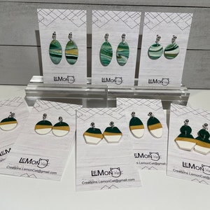 May include: Assortment of handmade polymer clay earrings in green, white and gold colours. The earrings are displayed on cards with the text "LEMON Creations LemonCat@gmail.com".
