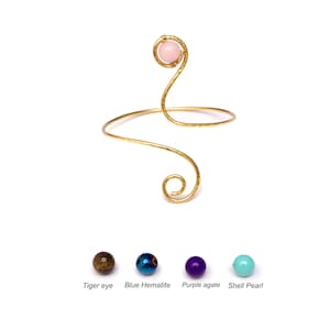May include: Gold wire bracelet with a pink stone bead.  The bracelet is shaped like a snake with a curled tail.  Four different colored beads are shown below the bracelet: tiger eye, blue hematite, purple agate, and shell pearl.