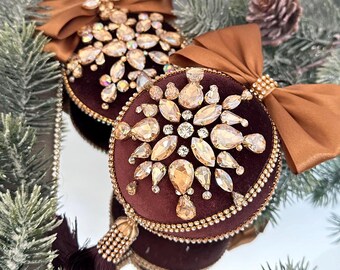 May include: Two brown velvet Christmas ornaments with gold trim and a large, sparkly, gold snowflake design. Each ornament has a brown satin bow.