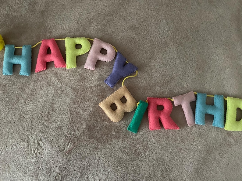 May include: A colorful felt banner that reads "Happy Birthday" with each letter in a different color. The banner is strung together with yellow string.