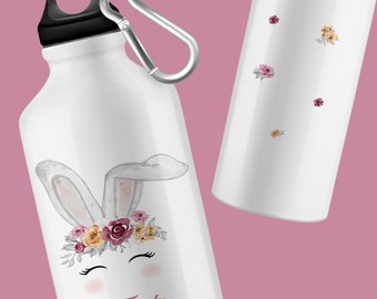 Könnte beinhalten: Weiße Aluminium-Wasserflasche mit schwarzem Deckel und Karabinerhaken. Die Flasche hat einen Blumengirlanden mit einem Hasengesicht und dem Namen "Jylia" darauf gedruckt.