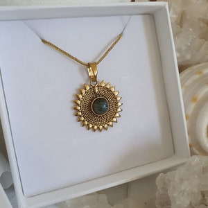 May include: A gold necklace with a pendant featuring a round, iridescent green gemstone surrounded by a sunburst design.