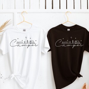May include: Two t-shirts, one white and one black, with the text "Happy Camper" and a small camper van graphic. Both shirts are hanging on hangers.
