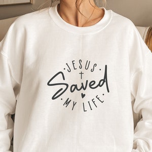 May include: White sweatshirt with a black graphic that says "Jesus Saved My Life" with a cross and a heart.