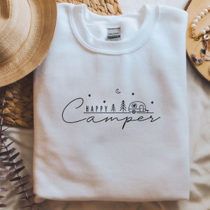 May include: White sweatshirt with a black graphic design that says "Happy Camper" with a camper van, trees, a moon, and stars.