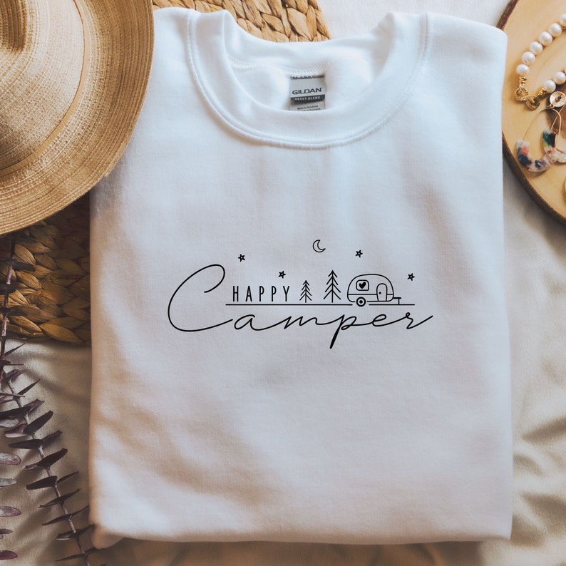 May include: White sweatshirt with a black graphic design that says "Happy Camper" with a camper van, trees, a moon, and stars.