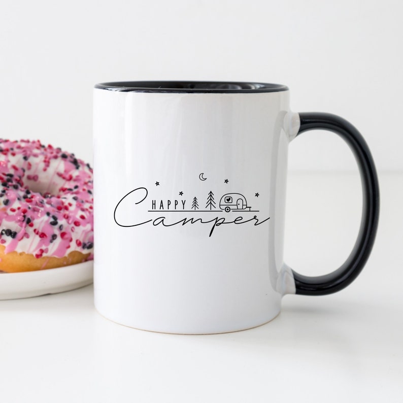 May include: White ceramic mug with a black rim and handle. The mug has a black graphic of a camper, trees, a moon, and stars with the text "Happy Camper" on it.