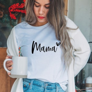Może przedstawiać: Biała koszulka z napisem "Mama" napisanym czarnym, ozdobnym pismem z małym sercem obok.