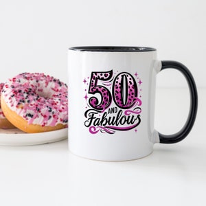 May include: White ceramic mug with a black rim and handle. The mug has a pink and black leopard print design with the text "50 and Fabulous".